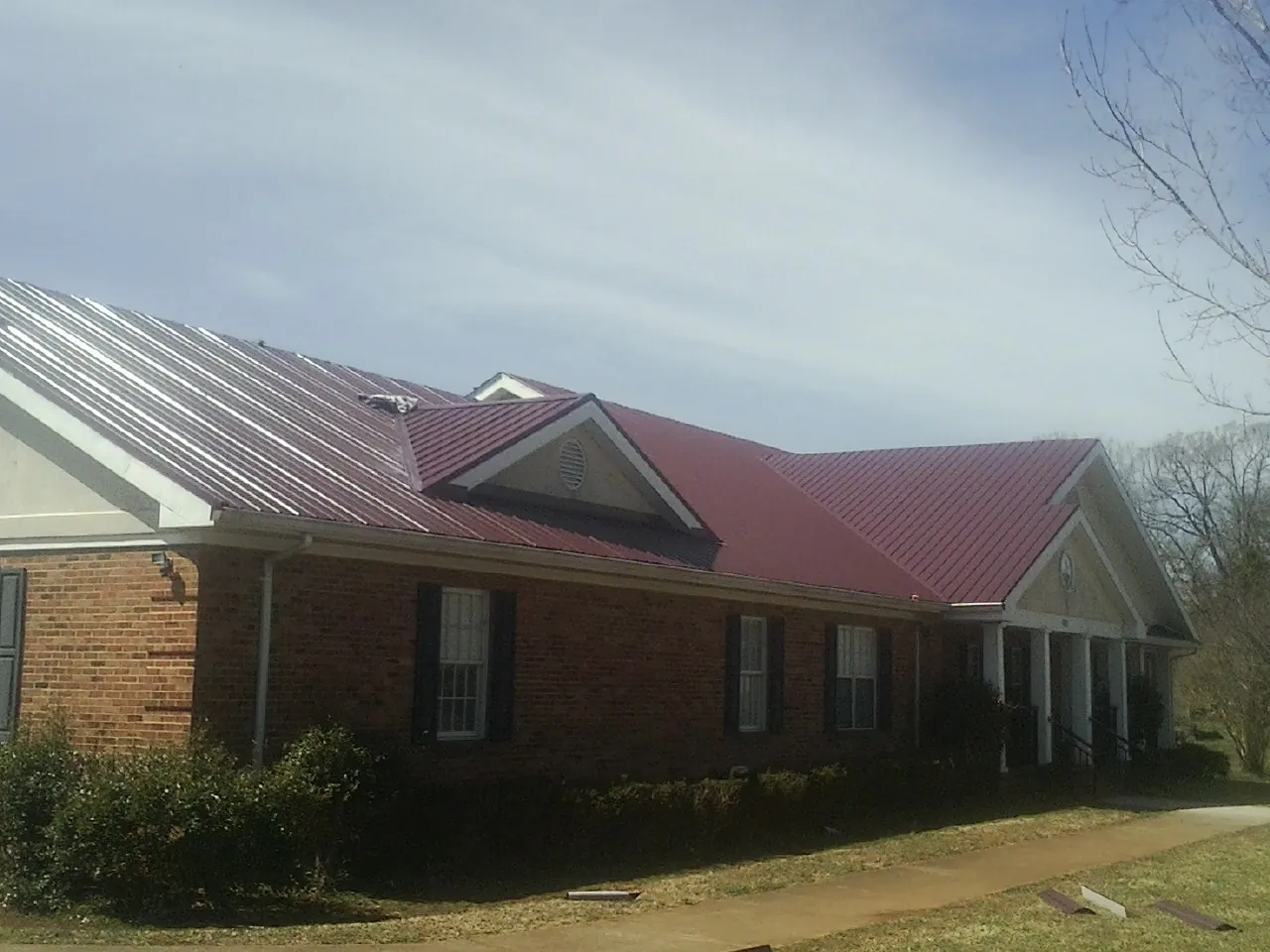 Red metal roof with gabled entries on a long brick building, from a Hail Damage Roof Repair job in Mantua