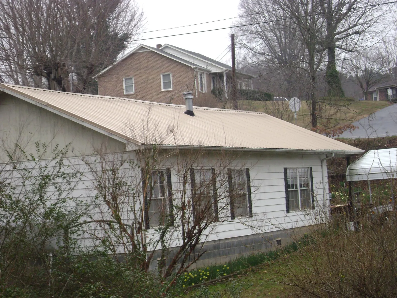 Tan metal roof on a white sided house set into a hillside — Commercial Roofing by Roofing Brothers in Mantua