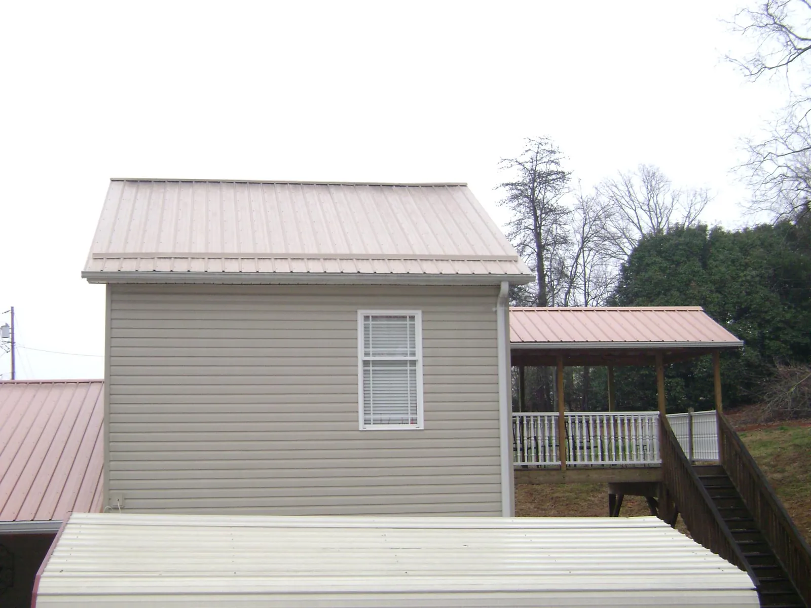 Tan metal roofs on a two story addition and attached porch, from a Roof Replacement job in Mantua